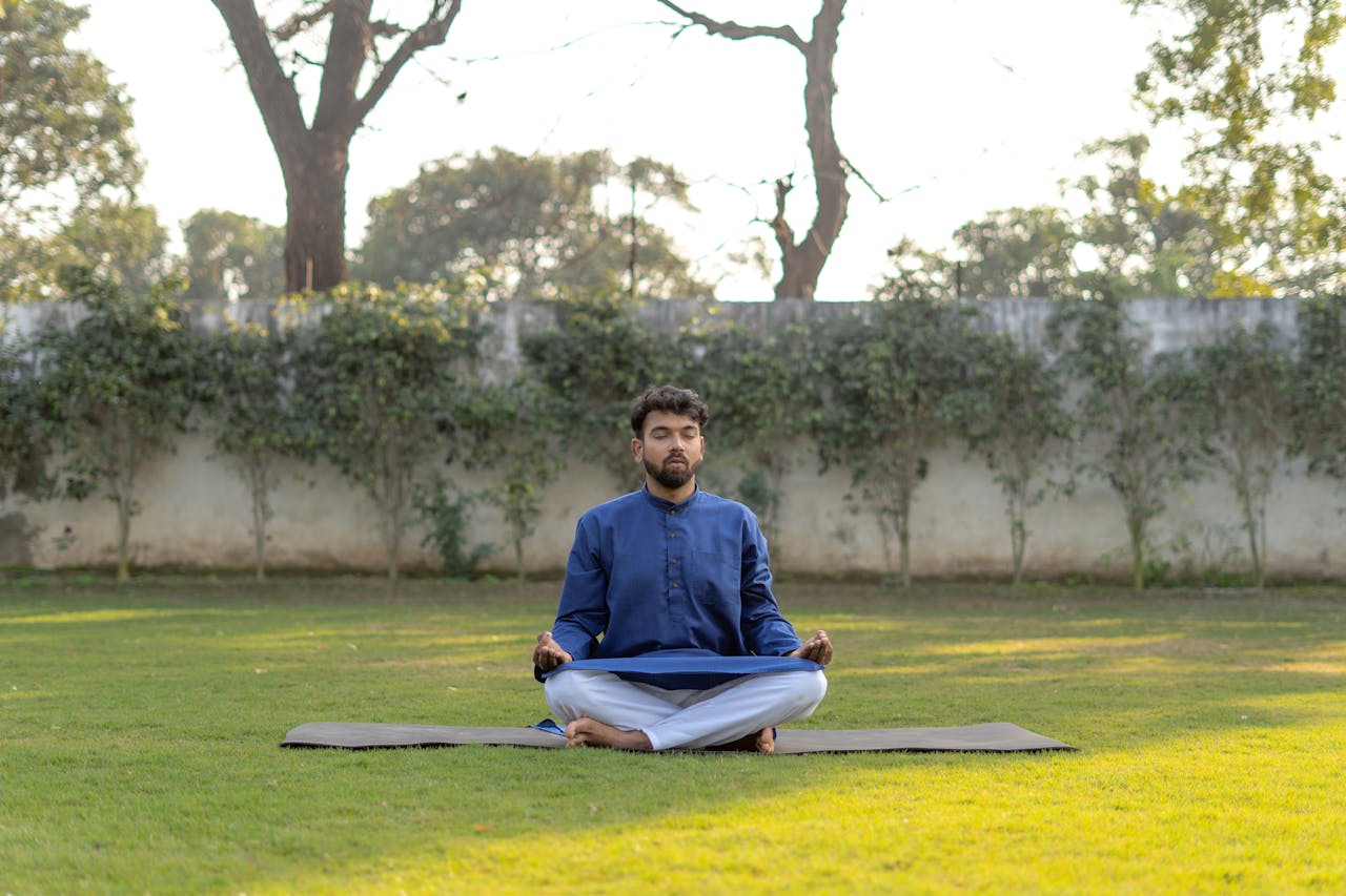 South Asian man meditating outdoors in a blue kurta, practicing yoga for wellness.