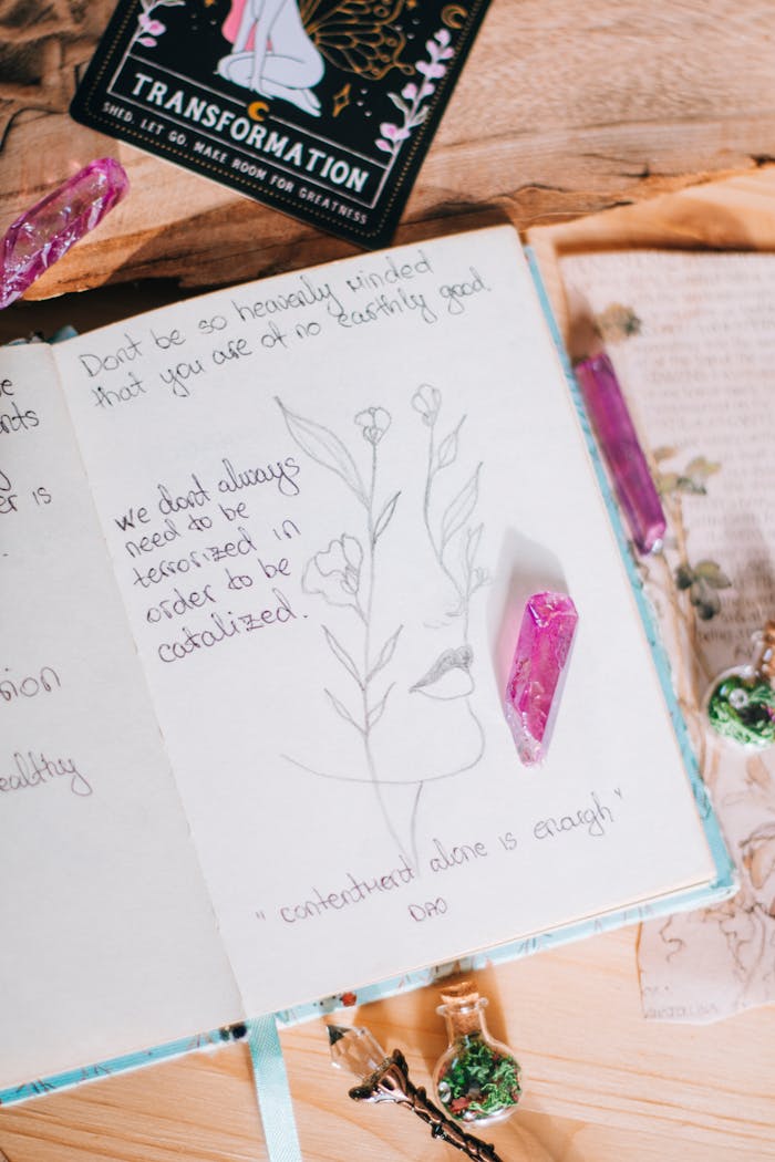 Open journal with esoteric writings, adorned with pink crystals and delicate sketches.