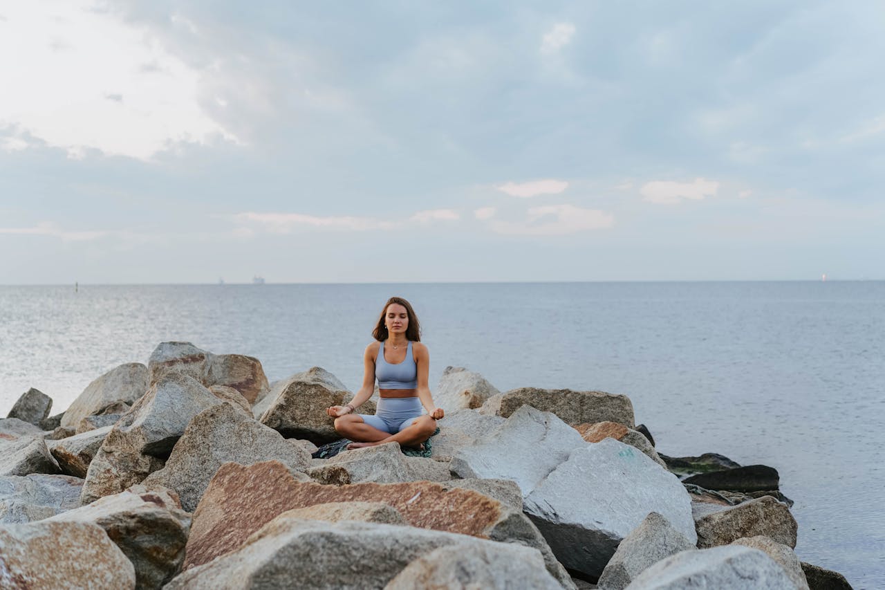 Serene scene of a woman meditating on rocks by the sea, embracing calmness and mindfulness.